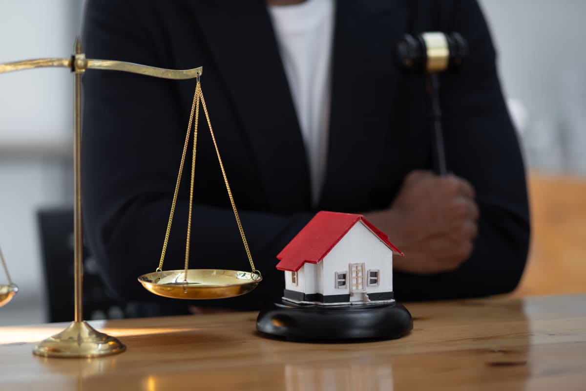 A man holding a gavel next to a small house and a scale
