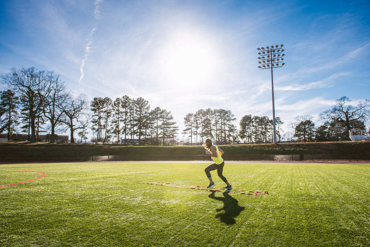 Young female athlete stepping between agility ladder on sports field